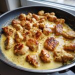 Close-up of seared chicken pieces simmering in a rich, creamy honey mustard sauce in a black skillet.