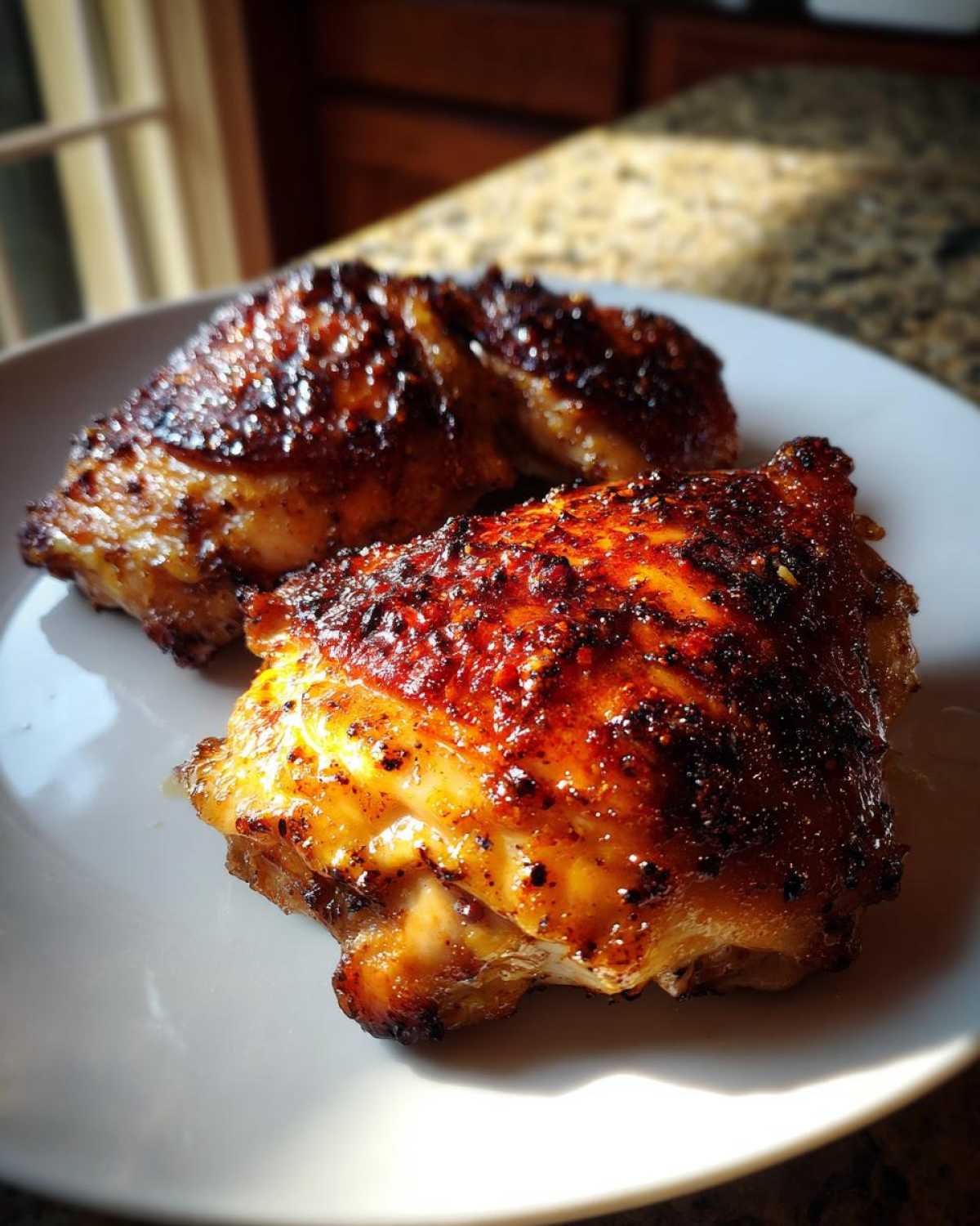 Two pieces of perfectly cooked Honey Mustard Chicken Thighs Oven Roasted with a dark, caramelized glaze on a white plate.