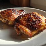 Two perfectly cooked, glazed Honey Mustard Chicken Thighs Oven Roasted resting on a white plate.