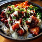 Close-up of a Honey Soy Chicken Bowl featuring glazed chicken pieces over white rice, drizzled with white sauce and green onions.