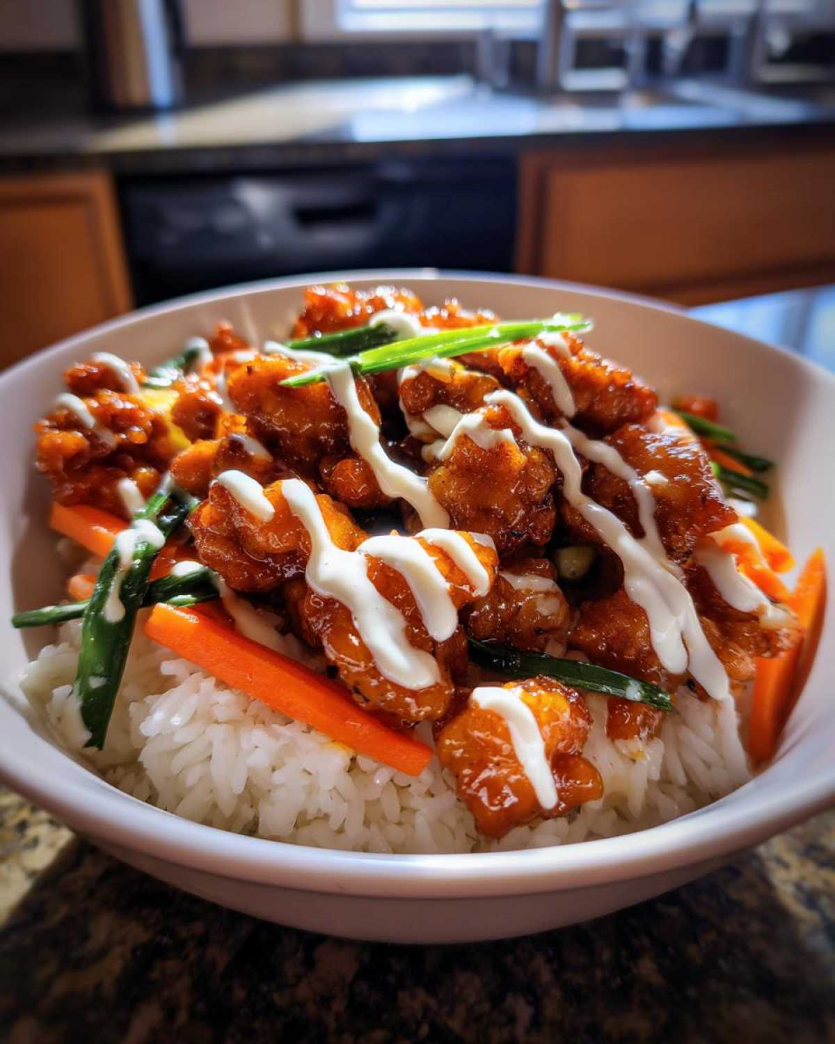 Close-up of a Honey Soy Chicken Bowl featuring crispy chicken pieces over rice, topped with a white garlic sauce drizzle and green onions.