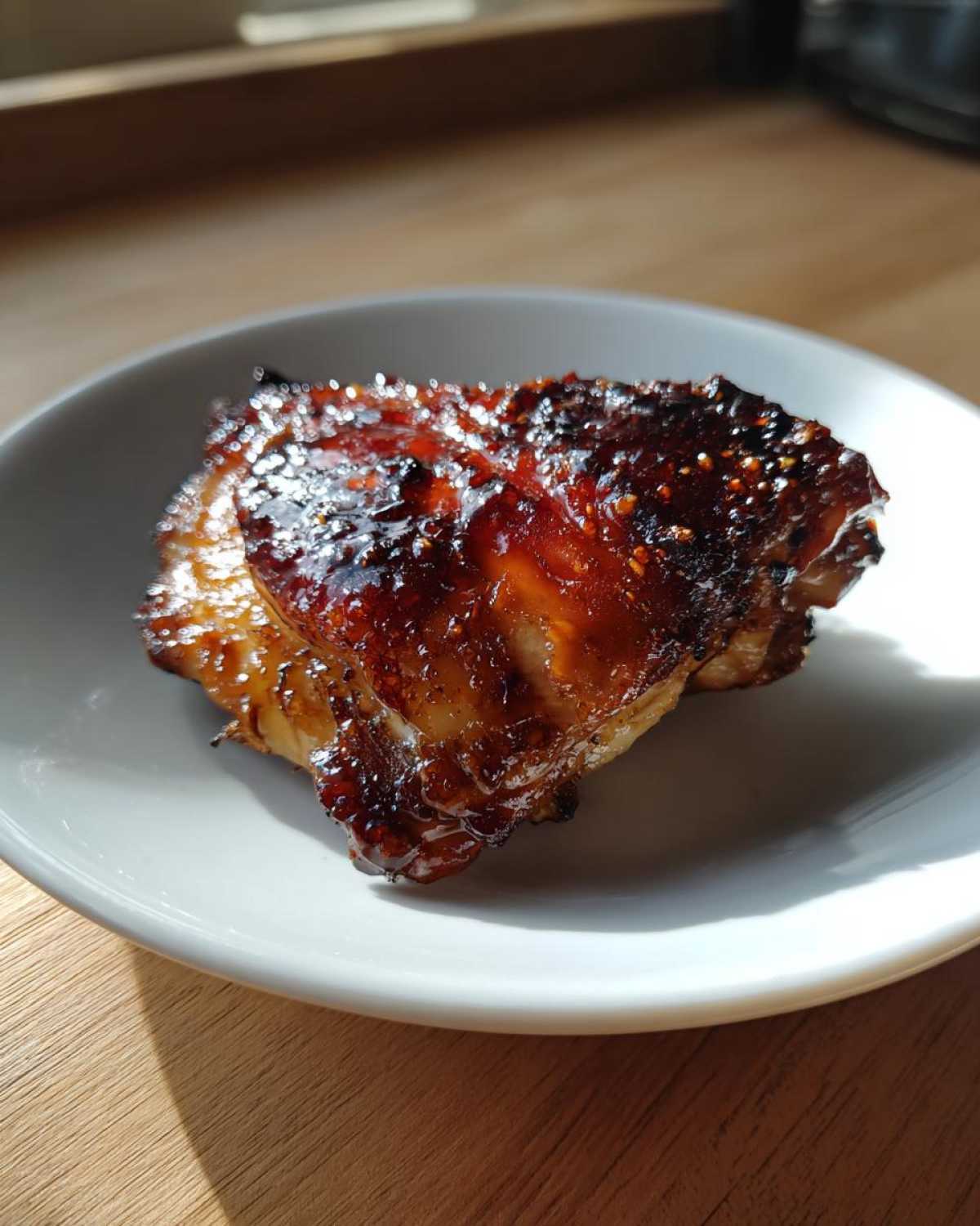 A single, perfectly glazed Honey Soy Chicken Thighs with crispy, caramelized edges on a white plate.