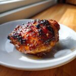 A close-up of a perfectly cooked Honey Soy Chicken Thighs with crispy, caramelized edges on a white plate.