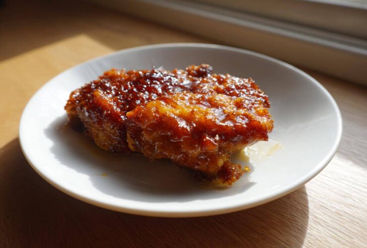 Two pieces of Honey Soy Chicken Thighs with Crispy Edges, glistening with a thick, dark glaze, served on a white plate.