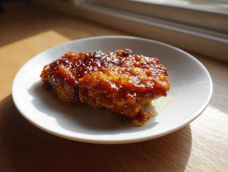 Two pieces of Honey Soy Chicken Thighs with Crispy Edges, glistening with a thick, dark glaze, served on a white plate.