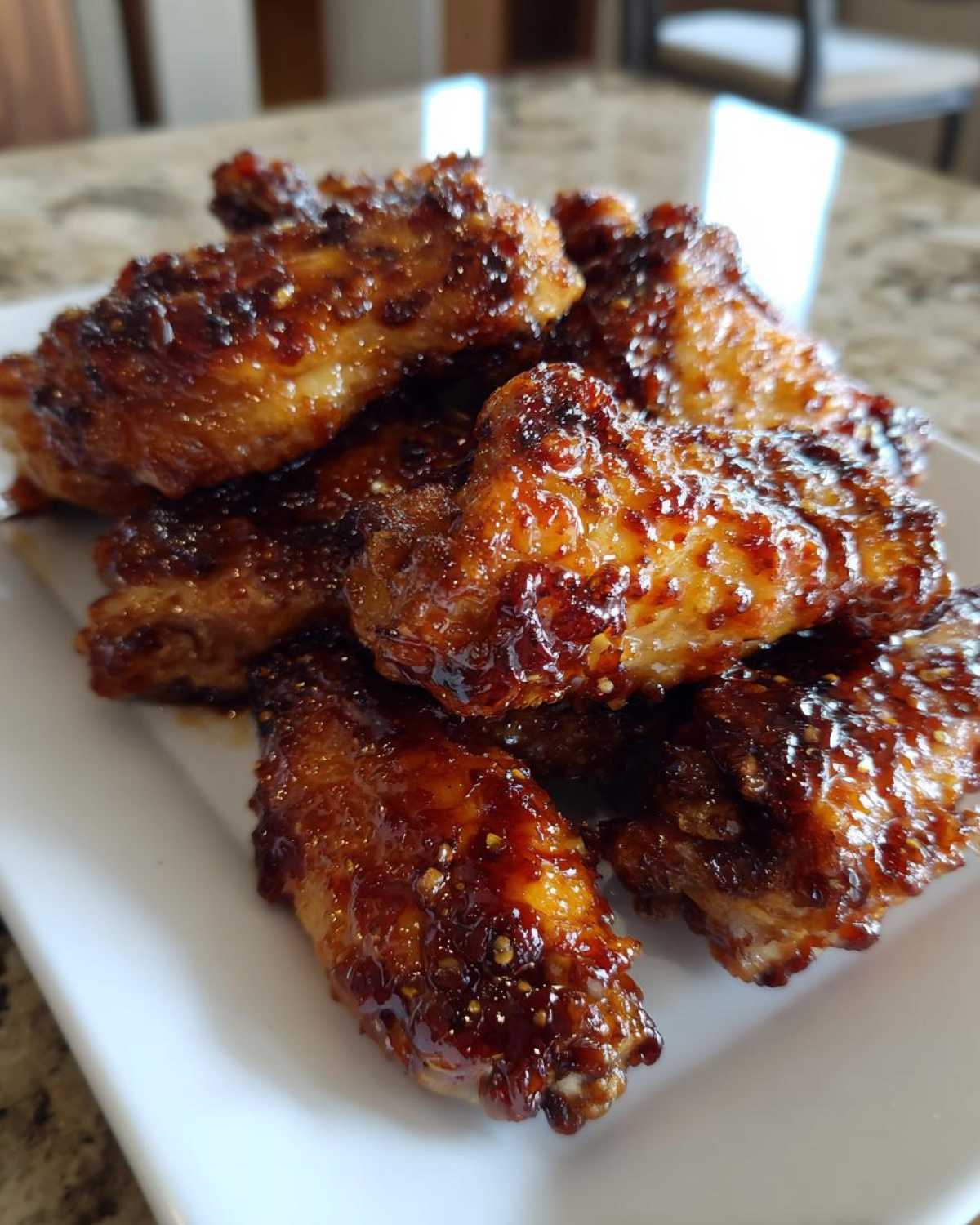 A close-up of a pile of crispy oven baked Honey Sriracha Chicken Wings coated in a sticky, dark glaze.