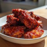A close-up of sticky and crispy Honey Sriracha Chicken Wings piled high in a white bowl.