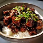 Close-up of a Sticky BBQ Chicken Bowl with Rice, featuring dark, glazed chicken pieces over white rice, topped with sesame seeds and green onions.