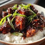 Close-up of a Sticky BBQ Chicken Bowl with Rice, topped with sesame seeds and green onions.