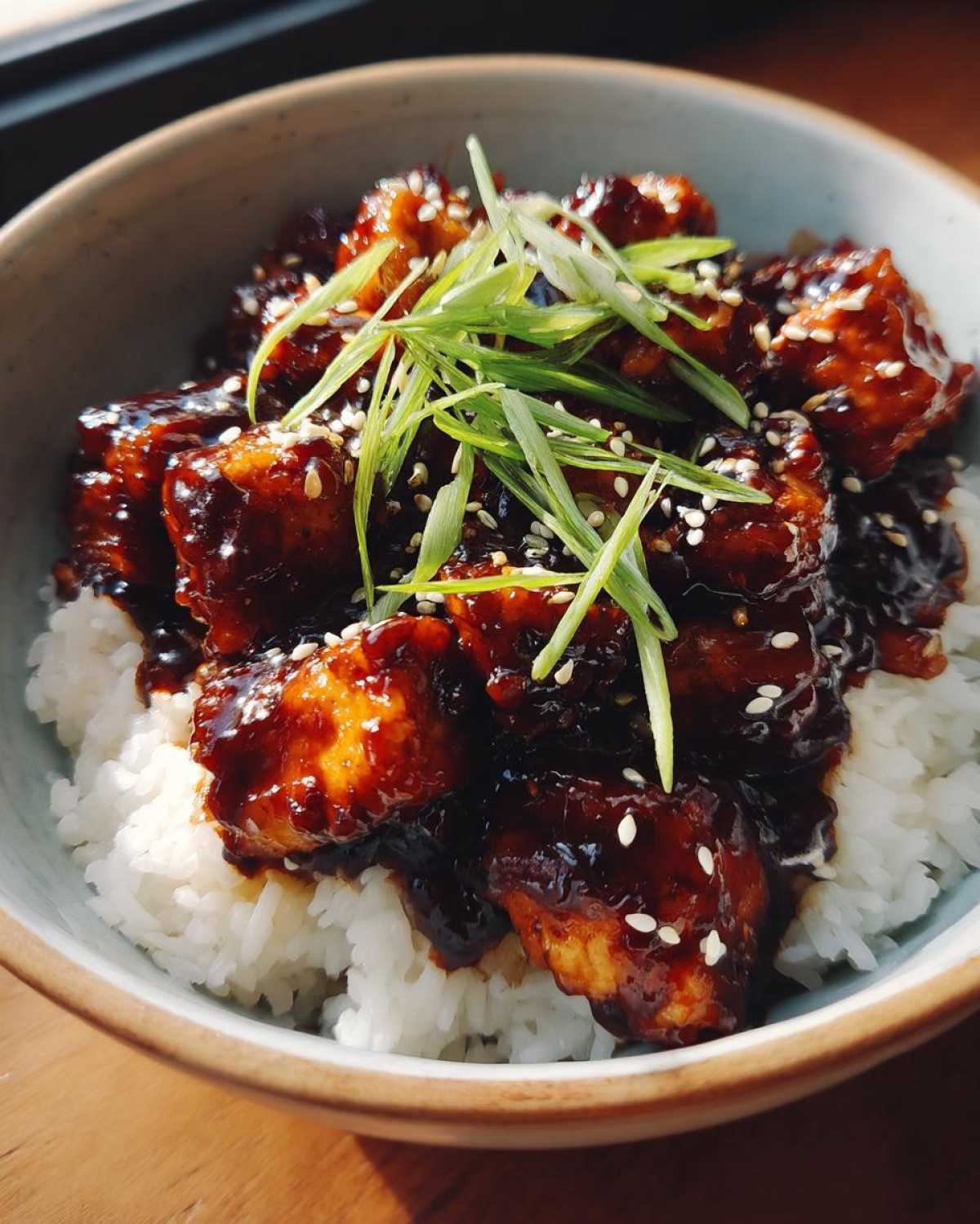 Close-up of a Sticky BBQ Chicken Bowl with Rice, topped with sesame seeds and green onions.