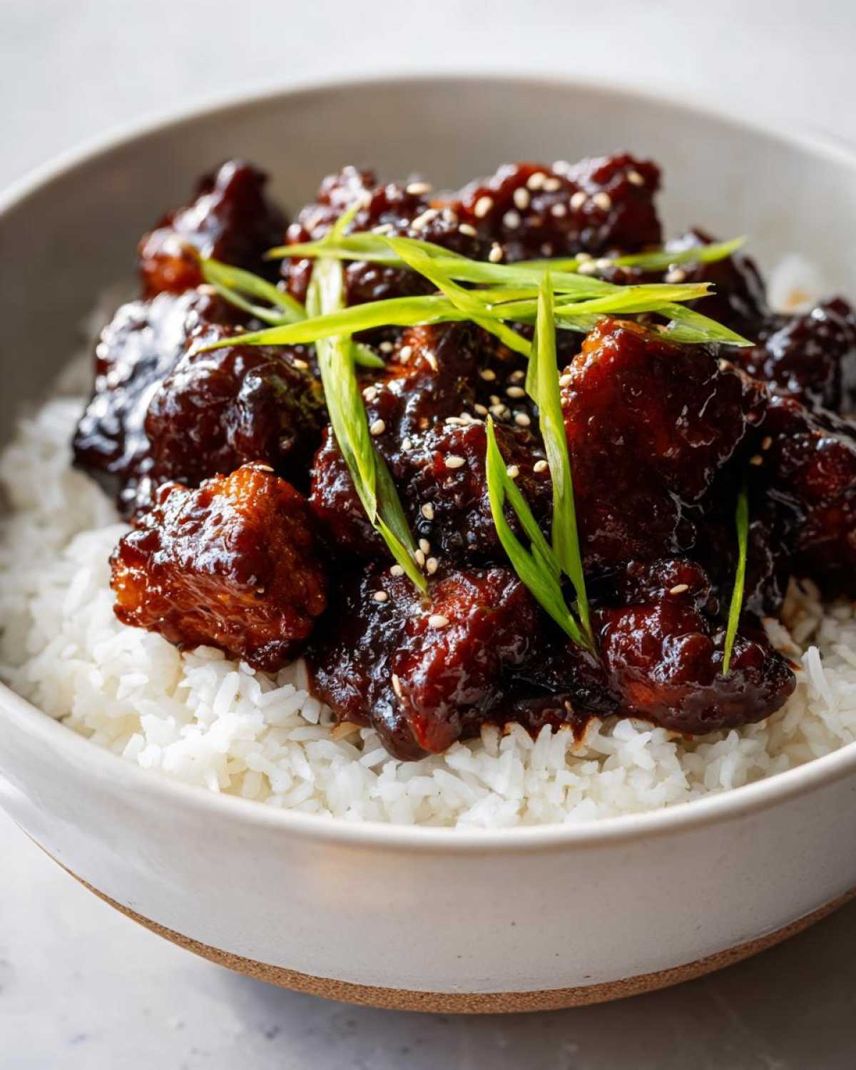Close-up of a Sticky BBQ Chicken Bowl with Rice, featuring dark glazed chicken pieces over white rice, garnished with sesame seeds and green onions.