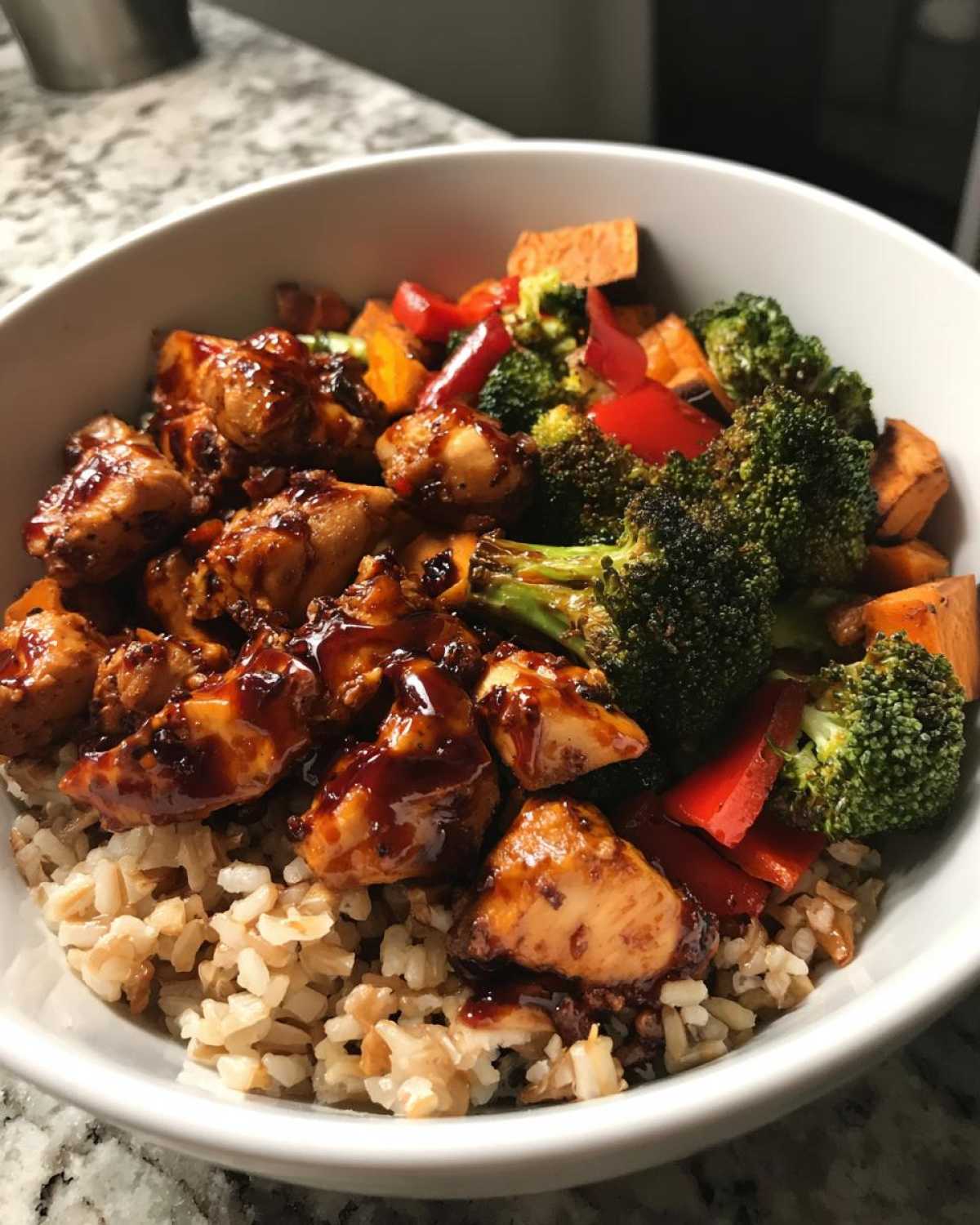 Close-up of a Sticky BBQ Chicken Bowl featuring glazed chicken pieces over brown rice with roasted broccoli, sweet potatoes, and red peppers.