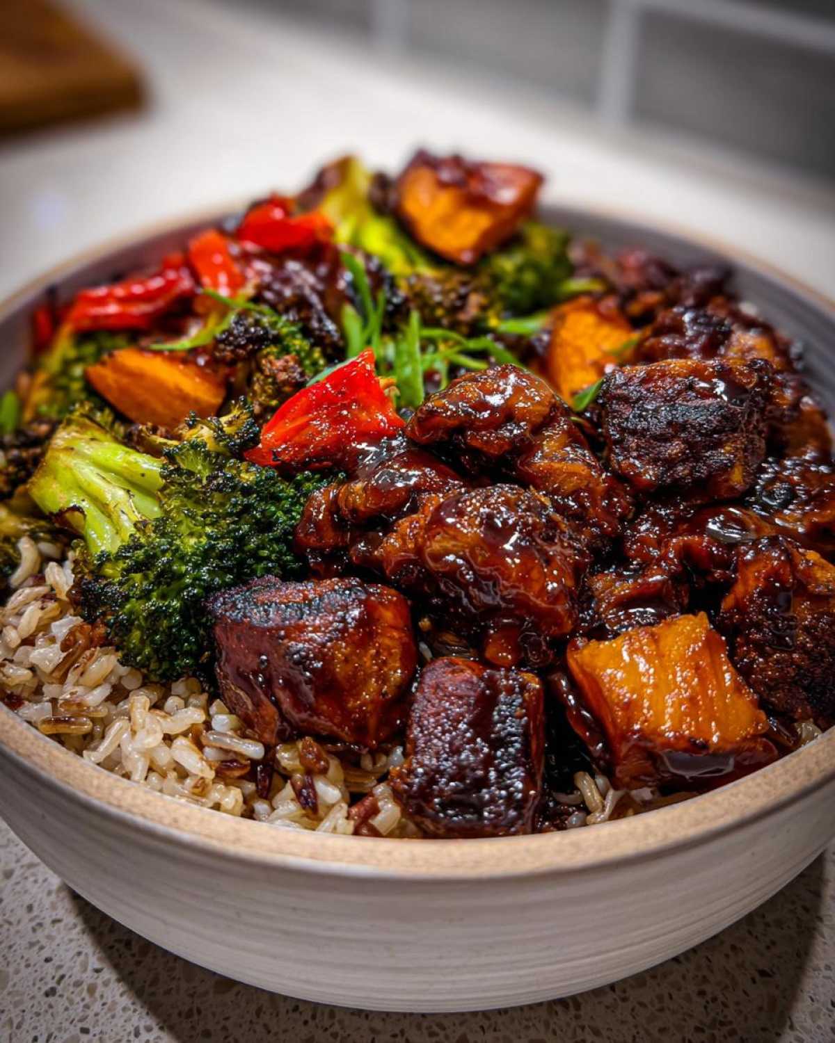 A close-up of a Sticky BBQ Chicken Bowl featuring glazed chicken pieces, roasted broccoli, sweet potatoes, and brown rice.