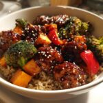 Close-up of a Sticky BBQ Chicken Bowl with brown rice, broccoli, sweet potato, and red peppers, topped with sesame seeds.