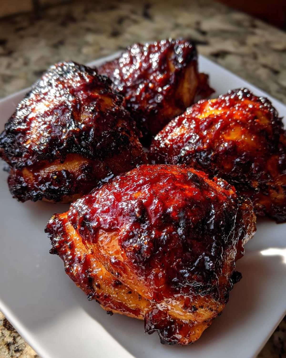 Four glistening Sticky BBQ Chicken Thighs with crispy, caramelized edges served on a white plate.