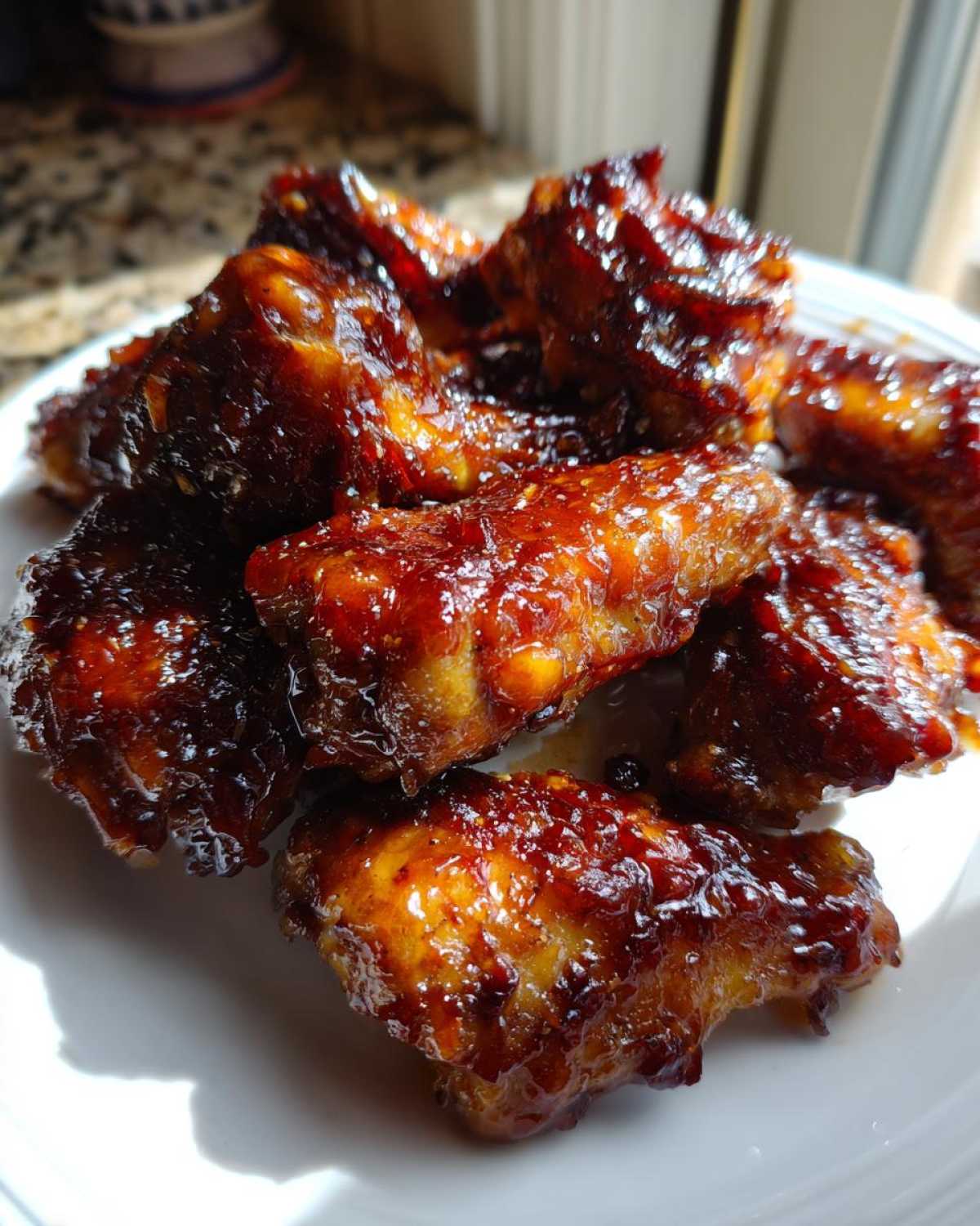 Close-up of sticky, glazed Honey Garlic Chicken Wings Oven Baked piled on a white plate.
