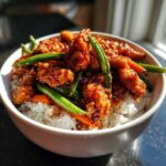 Close-up of a white bowl filled with white rice topped with saucy Sticky Orange Chicken Bowl with Rice and Veggies and bright green beans.