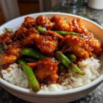 Close-up of a white bowl filled with Sticky Orange Chicken Bowl with Rice and Veggies, featuring glazed chicken pieces and bright green snap peas.