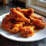 A pile of crispy oven-baked Sticky Orange Chicken Wings coated in a shiny glaze, served on a white plate.