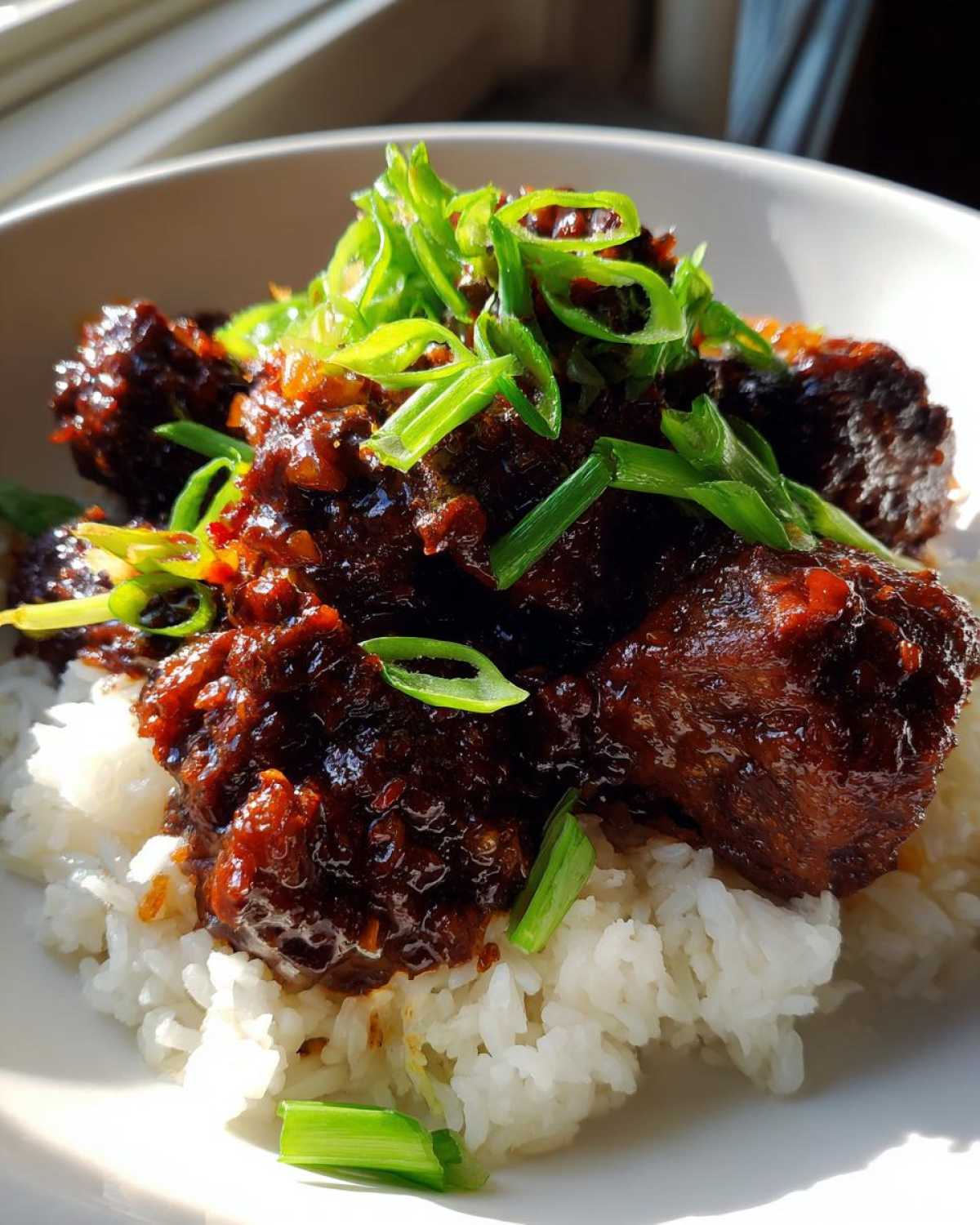 Close-up of Sticky Sweet Chili Chicken Skillet pieces coated in dark sauce, served over white rice and topped with fresh green onions.