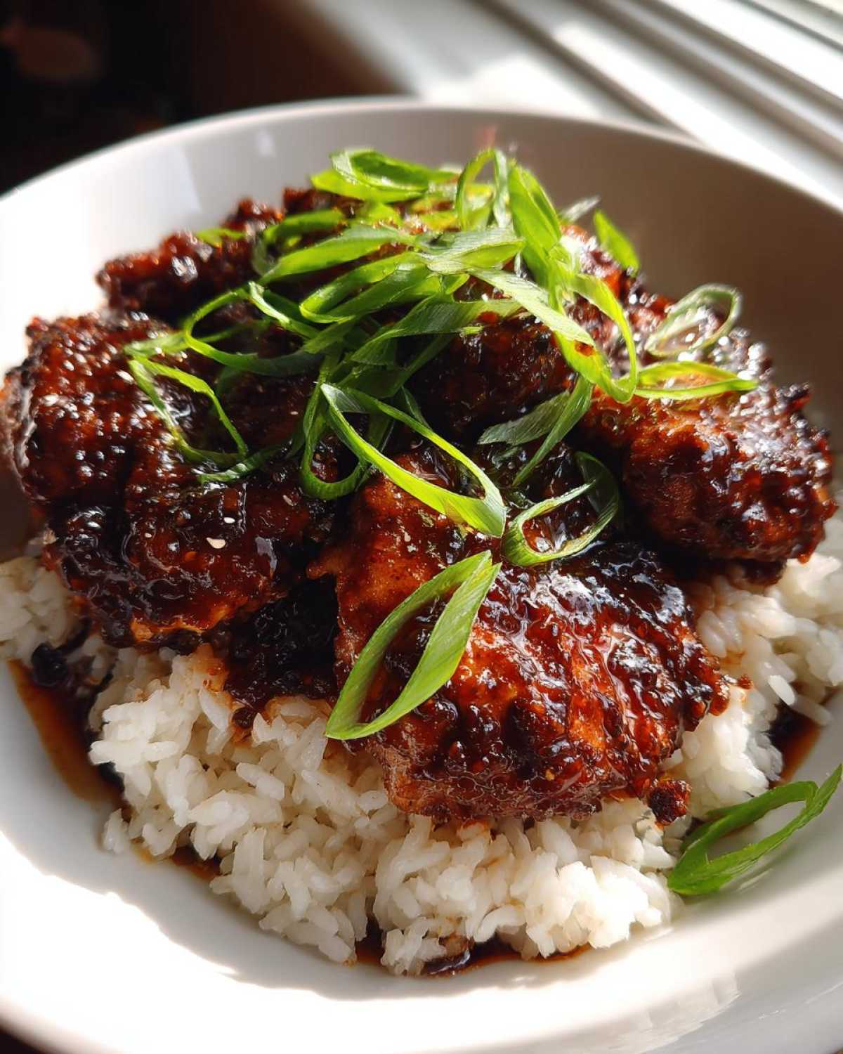 Close-up of Sticky Sweet Chili Chicken Skillet pieces coated in dark glaze served over white rice and topped with scallions.