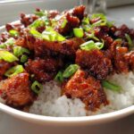 Close-up of Sticky Sweet Chili Chicken Skillet pieces coated in glossy sauce served over fluffy white rice and garnished with green onions.