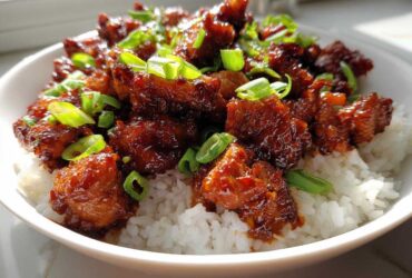 Close-up of Sticky Sweet Chili Chicken Skillet pieces coated in glossy sauce served over fluffy white rice and garnished with green onions.