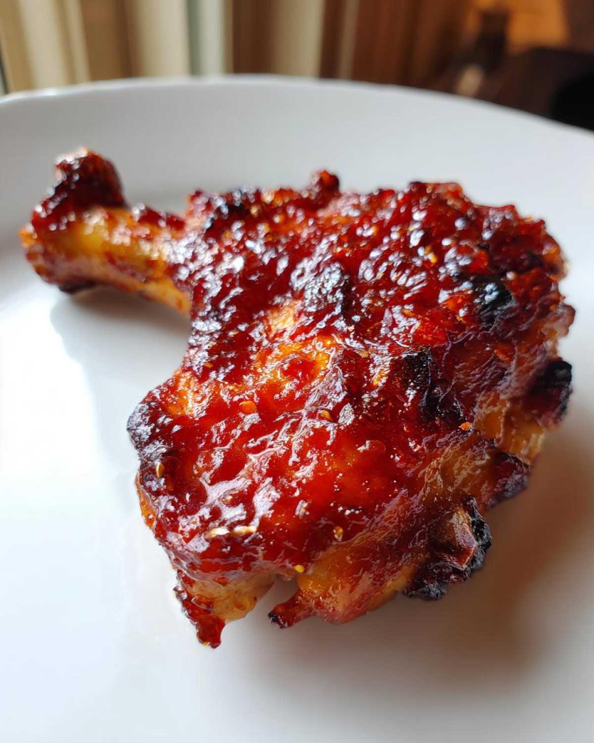 Close-up of a single, glossy, oven-baked chicken thigh coated in sticky sweet chili glaze.