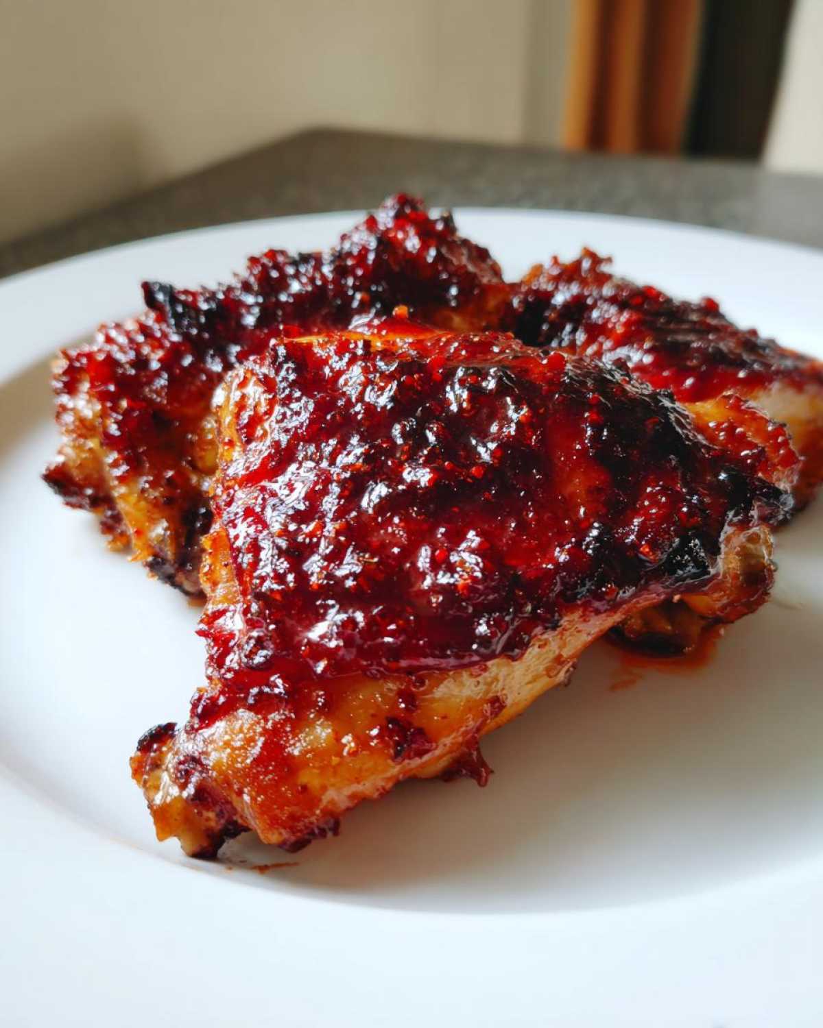 Close-up of three oven-baked Sticky Sweet Chili Chicken Thighs coated in a thick, glossy, dark red glaze.