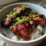 Close-up of Sticky Sweet Chili Chicken Thighs coated in a dark, glossy sauce, served over white rice and topped with sliced green onions.