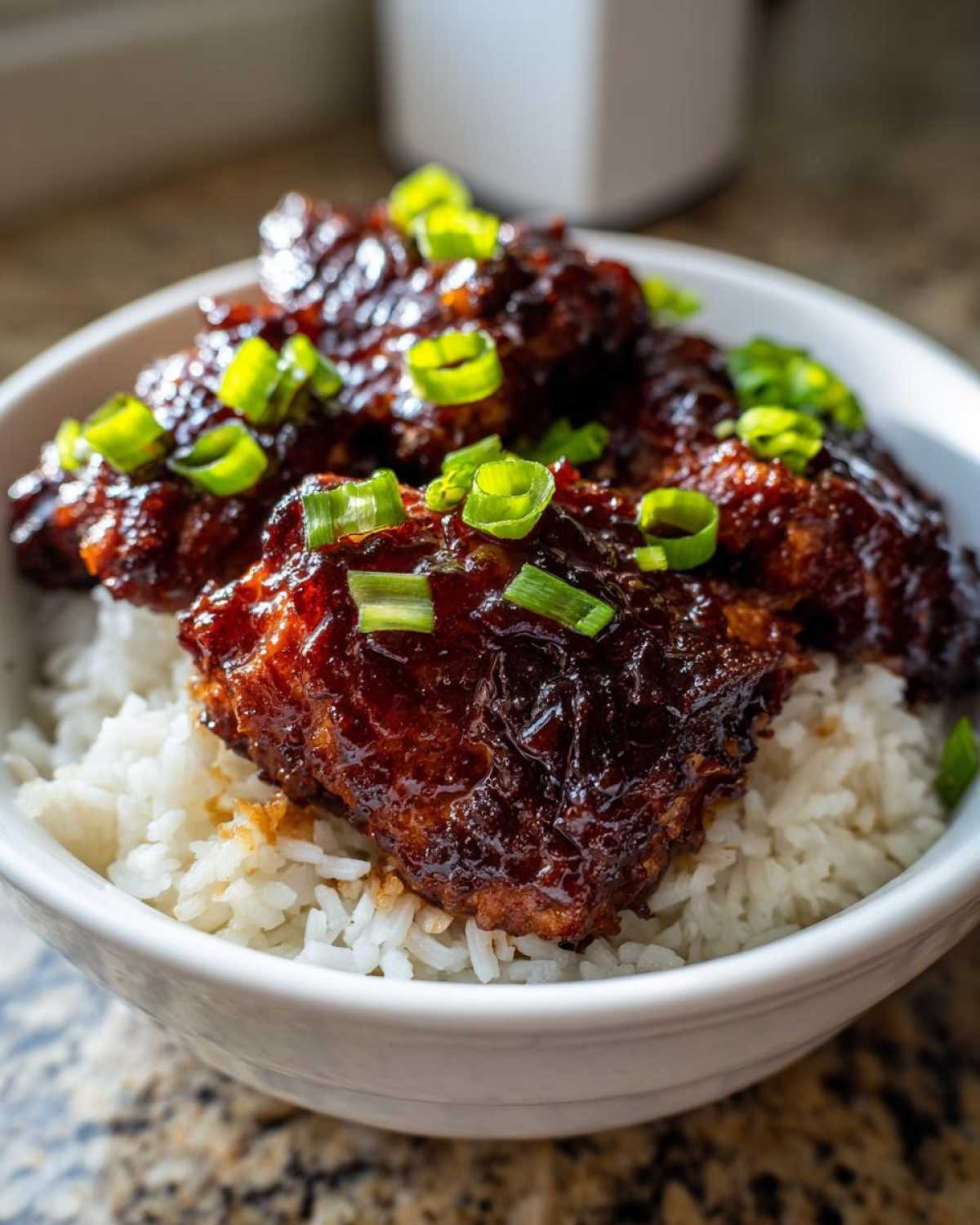 Close-up of Sticky Sweet Chili Chicken Thighs coated in dark glaze, served over white rice and topped with sliced green onions.