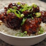 Close-up of Sticky Sweet Chili Chicken Thighs coated in a dark, glossy sauce, served over white rice and topped with sliced green onions.