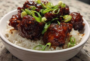 Close-up of Sticky Sweet Chili Chicken Thighs coated in a dark, glossy sauce, served over white rice and topped with sliced green onions.