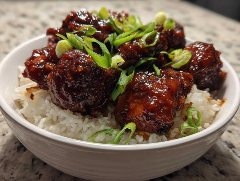 Close-up of Sticky Sweet Chili Chicken Thighs coated in a dark, glossy sauce, served over white rice and topped with sliced green onions.