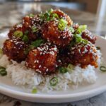 A mound of Sticky Teriyaki Chicken Bites coated in glossy sauce, topped with sesame seeds and green onions, served over white rice.