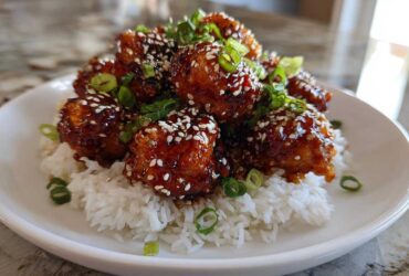 A mound of Sticky Teriyaki Chicken Bites coated in glossy sauce, topped with sesame seeds and green onions, served over white rice.