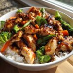 A close-up of a white bowl filled with Sticky Teriyaki Chicken Bowl with Rice and Veggies, topped with glossy sauce and sesame seeds.