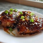 Two pieces of glazed Sticky Teriyaki Chicken Thighs with Garlic, topped with sesame seeds and chopped green onions.