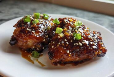 Two pieces of glazed Sticky Teriyaki Chicken Thighs with Garlic, topped with sesame seeds and chopped green onions.