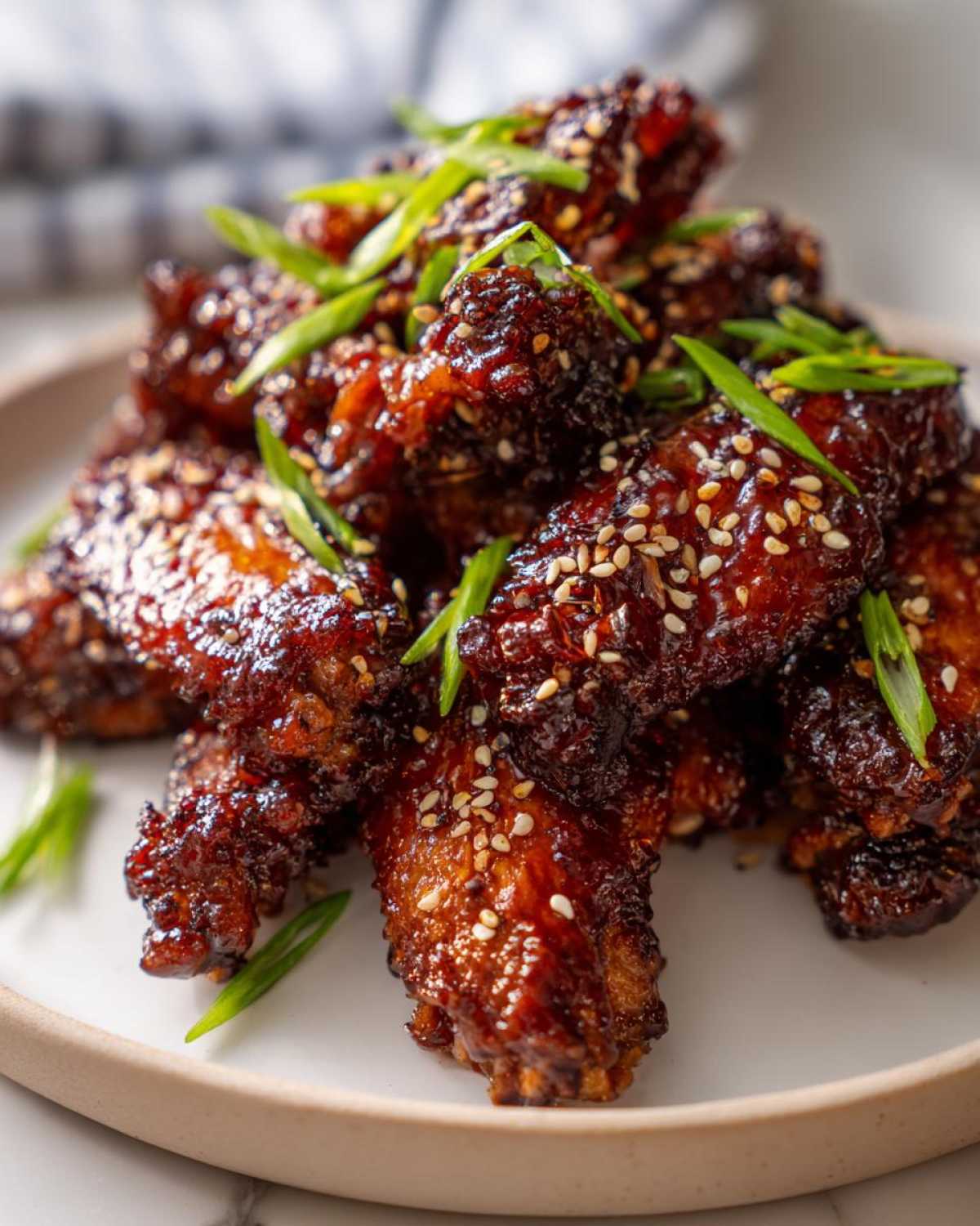 Close-up of crispy oven baked Sticky Teriyaki Chicken Wings coated in dark glaze, topped with sesame seeds and green onions.