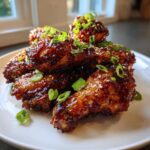 A close-up of glossy Sticky Teriyaki Chicken Wings Oven Baked, garnished with sesame seeds and sliced green onions.