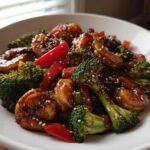 Close-up of Sticky Teriyaki Shrimp Stir Fry Quick Meal with broccoli and red peppers, garnished with sesame seeds.