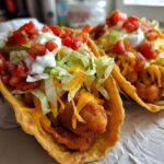 Two fully loaded Air Fried Fish Walking Tacos featuring crispy fish, shredded lettuce, cheese, salsa, and sour cream.