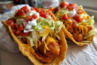 Two fully loaded Air Fried Fish Walking Tacos featuring crispy fish, shredded lettuce, cheese, salsa, and sour cream.