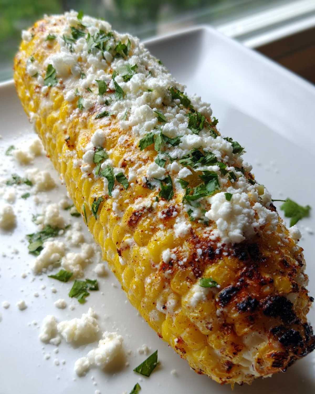 A perfectly cooked Air Fryer Corn on the Cob topped generously with crumbled white cheese and fresh cilantro.