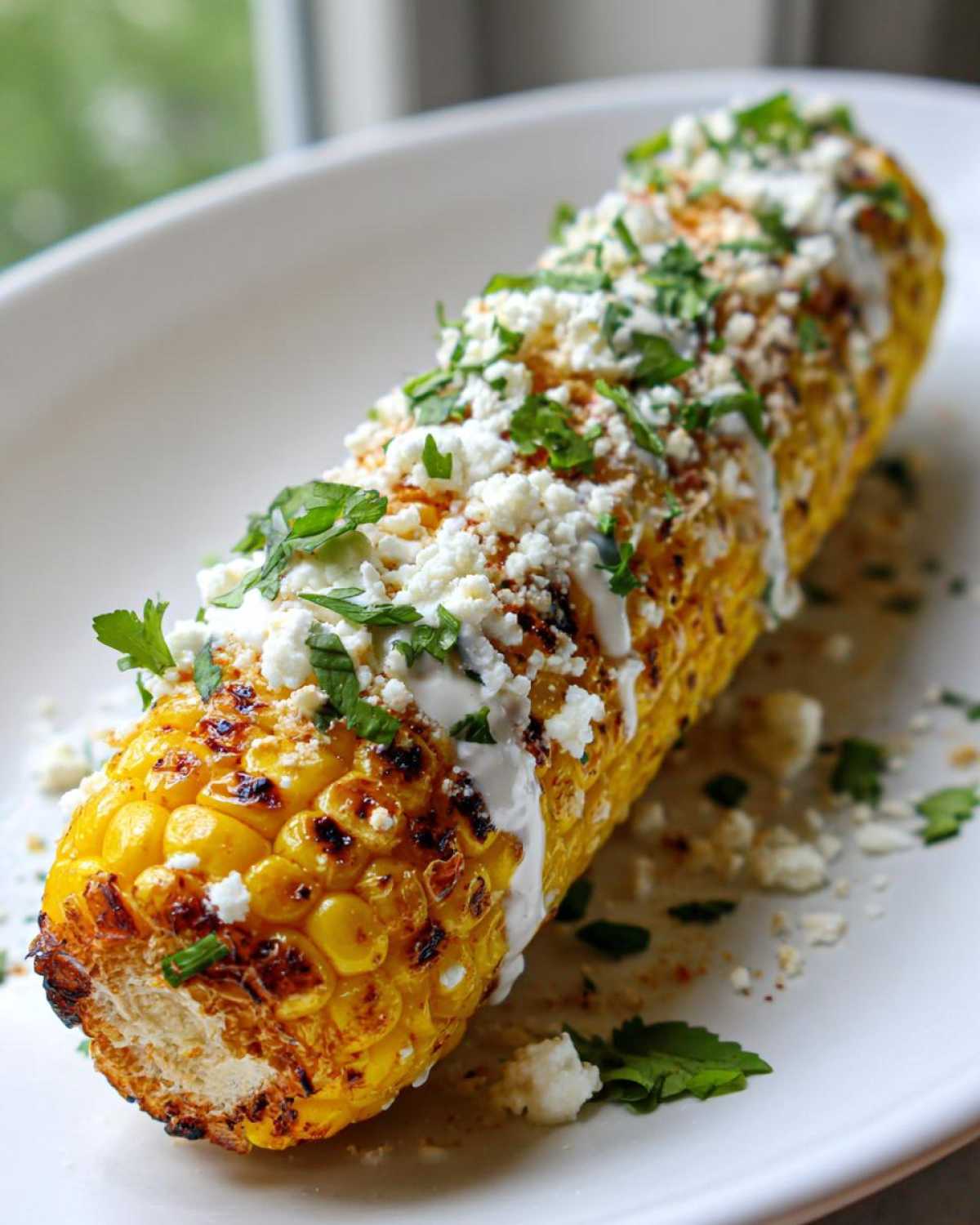 Close-up of a fully cooked Air Fryer Corn on the Cob topped with cotija cheese, cream sauce, and cilantro.