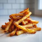 A tall pile of golden brown, crispy Air Fryer French Fries sprinkled generously with coarse salt.
