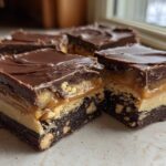 Close-up of several squares of Amazing Snickers Fudge showing distinct layers: chocolate topping, caramel/peanuts, peanut butter, and a dense brownie base.