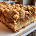 A close-up, mouth-watering shot of a single serving of Apple Bars featuring a thick layer of spiced apple filling and a crunchy oat crumb topping.