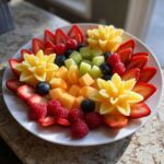 A stunning Baby Bloom Fruit Platter centerpiece featuring carved pineapple flowers, strawberries, raspberries, blueberries, cantaloupe, and honeydew.